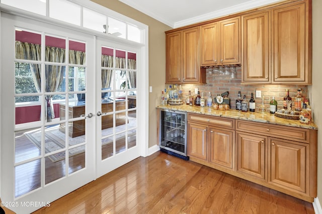 bar with a dry bar, light wood finished floors, tasteful backsplash, ornamental molding, and beverage cooler