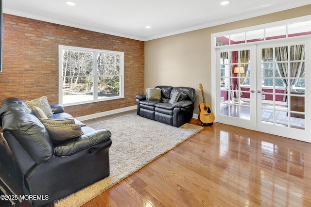 living room featuring baseboards, brick wall, wood finished floors, crown molding, and french doors