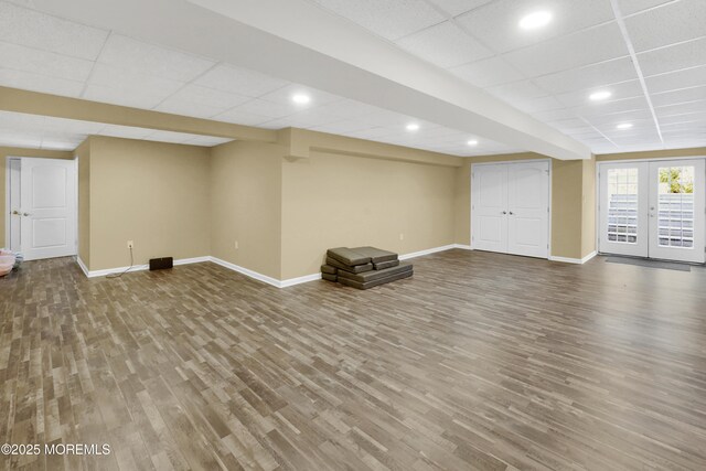 basement featuring baseboards, a drop ceiling, wood finished floors, and french doors