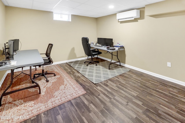 office space with a paneled ceiling, a wall mounted air conditioner, baseboards, and wood finished floors