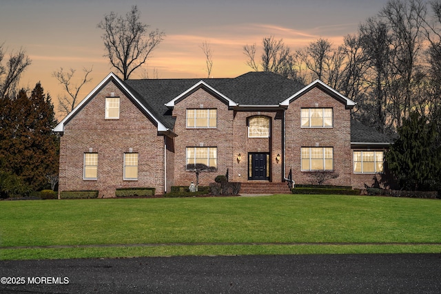 traditional home featuring brick siding, a shingled roof, and a front yard