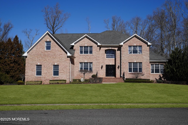 traditional-style home featuring a shingled roof, a front yard, and brick siding