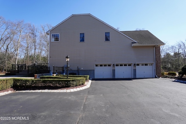 view of side of property featuring driveway, a shingled roof, and an attached garage