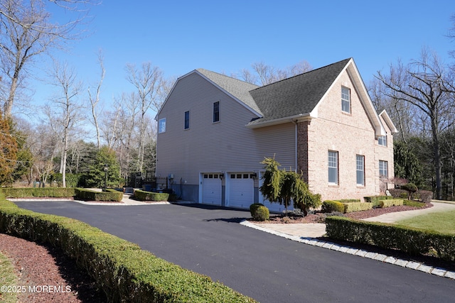 view of home's exterior with an attached garage, roof with shingles, aphalt driveway, and brick siding