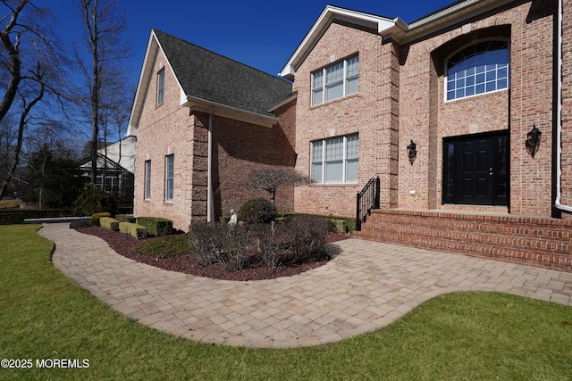 view of side of property featuring brick siding, a lawn, and roof with shingles