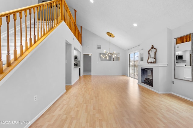 unfurnished living room with light wood-style flooring, stairway, a glass covered fireplace, a chandelier, and baseboards