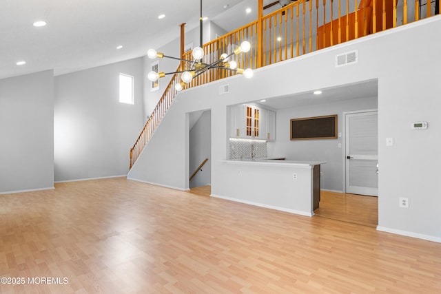 unfurnished living room with a chandelier, light wood-type flooring, visible vents, and baseboards