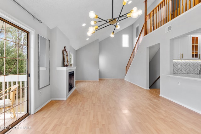 unfurnished living room with baseboards, visible vents, light wood-style floors, a fireplace, and a chandelier