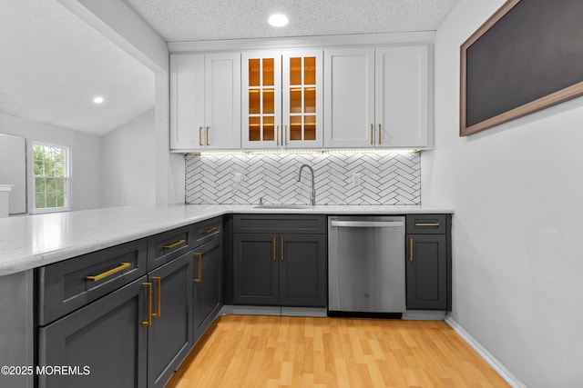 kitchen featuring a sink, light wood-style floors, white cabinets, stainless steel dishwasher, and decorative backsplash