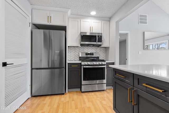 kitchen featuring stainless steel appliances, light countertops, visible vents, white cabinetry, and light wood-type flooring