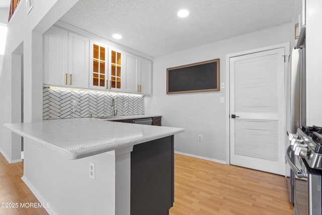 kitchen featuring stainless steel appliances, white cabinetry, light wood-style floors, and a peninsula