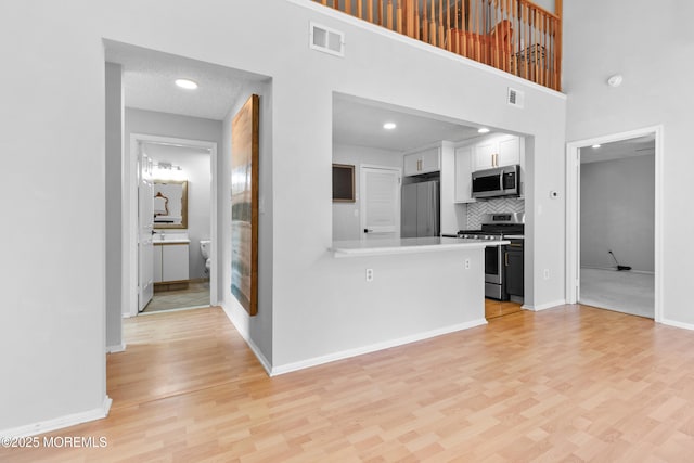 kitchen with stainless steel appliances, light wood-type flooring, white cabinets, and visible vents