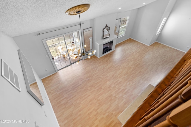 living room featuring a fireplace, visible vents, a textured ceiling, wood finished floors, and baseboards