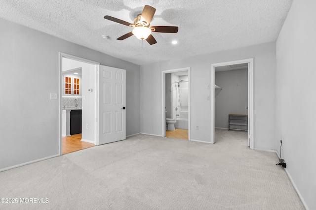 unfurnished bedroom with a textured ceiling, connected bathroom, baseboards, carpet, and a walk in closet