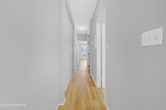 corridor featuring light wood finished floors and baseboards