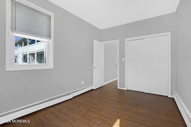 unfurnished bedroom featuring a baseboard heating unit, a closet, wood finished floors, and baseboards