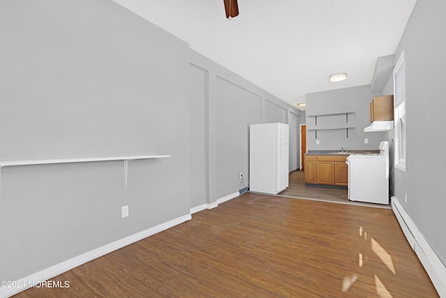 unfurnished living room with baseboard heating, dark wood finished floors, a ceiling fan, and baseboards