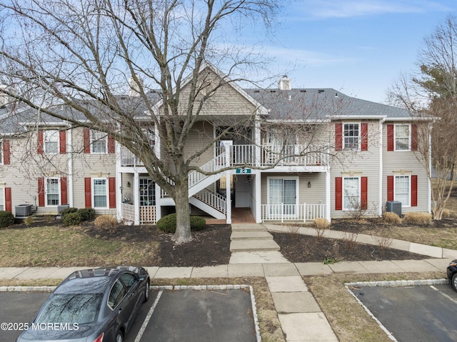 view of front of house with uncovered parking, a chimney, a balcony, and central air condition unit