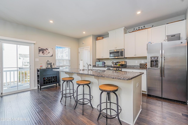 kitchen with a breakfast bar area, stone counters, dark wood-style flooring, appliances with stainless steel finishes, and an island with sink