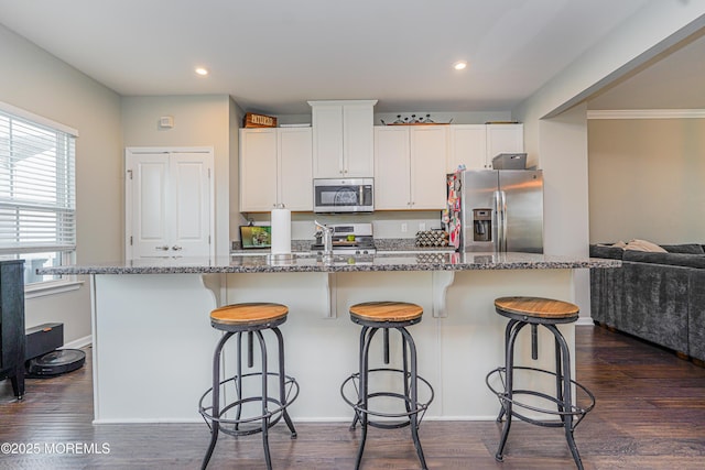 kitchen featuring appliances with stainless steel finishes, stone counters, dark wood finished floors, and a center island with sink