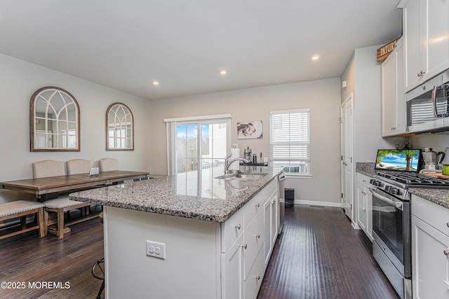 kitchen featuring light stone counters, stainless steel appliances, a sink, white cabinets, and dark wood finished floors