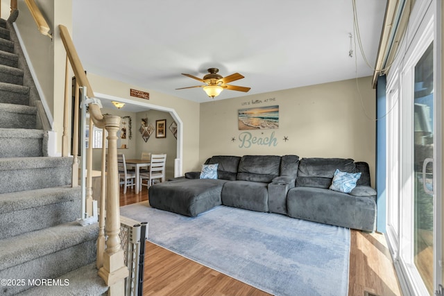 living area with stairs, wood finished floors, arched walkways, and ceiling fan