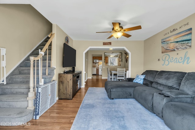 living room featuring baseboards, stairs, wood finished floors, arched walkways, and a ceiling fan