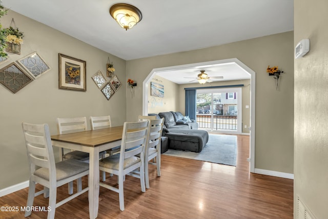 dining room featuring arched walkways, baseboards, and wood finished floors