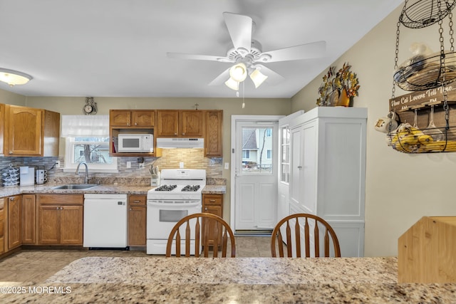 kitchen with brown cabinets, under cabinet range hood, a sink, white appliances, and decorative backsplash