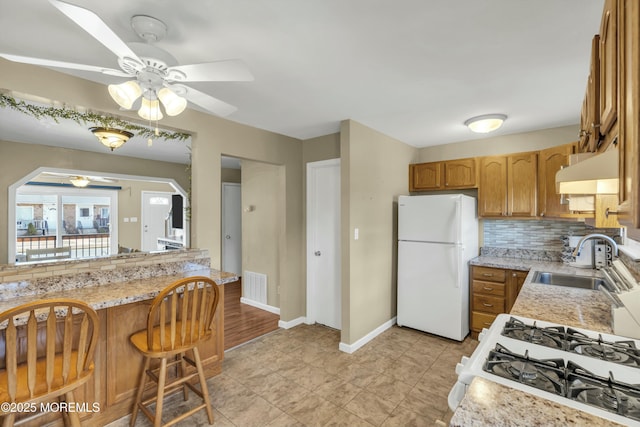 kitchen featuring visible vents, a sink, under cabinet range hood, backsplash, and white appliances