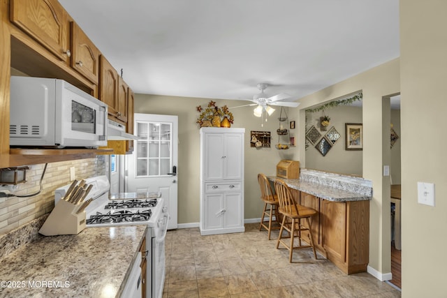 kitchen with tasteful backsplash, brown cabinets, white appliances, and baseboards