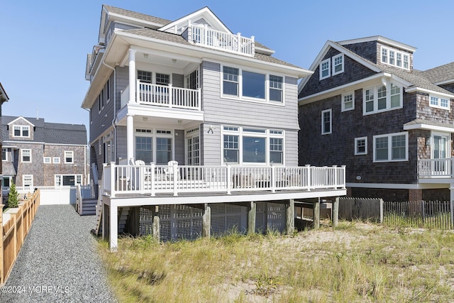 back of property with a shingled roof, fence, and a balcony