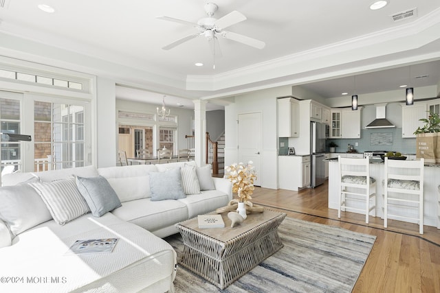 living area featuring ceiling fan with notable chandelier, ornamental molding, stairway, and light wood-style flooring