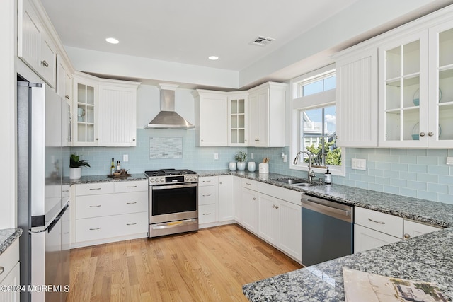 kitchen with light wood-style flooring, a sink, white cabinets, appliances with stainless steel finishes, and wall chimney exhaust hood