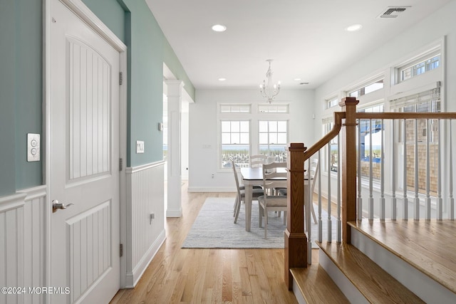 dining room featuring a wainscoted wall, visible vents, light wood finished floors, an inviting chandelier, and ornate columns