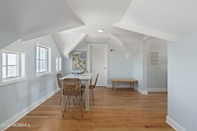 dining room featuring light wood-type flooring, visible vents, lofted ceiling, and baseboards