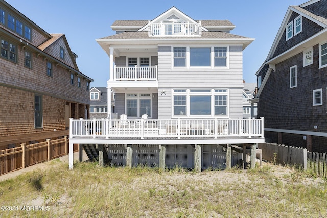 rear view of house featuring roof with shingles, fence, and a balcony