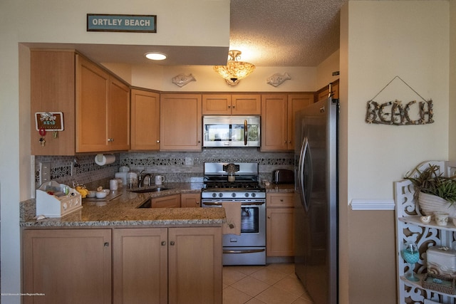 kitchen featuring light tile patterned floors, a peninsula, a sink, stainless steel appliances, and backsplash