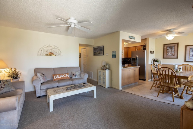 living area featuring visible vents, ceiling fan, light carpet, light tile patterned floors, and a textured ceiling