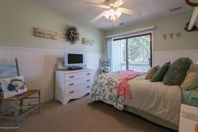 bedroom with access to exterior, visible vents, light colored carpet, wainscoting, and a textured ceiling