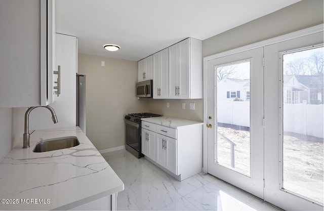 kitchen featuring white cabinets, light stone countertops, marble finish floor, stainless steel appliances, and a sink