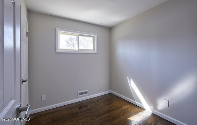 empty room featuring dark wood-style floors, visible vents, and baseboards