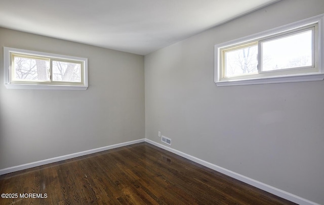 empty room featuring plenty of natural light, visible vents, baseboards, and dark wood-style flooring