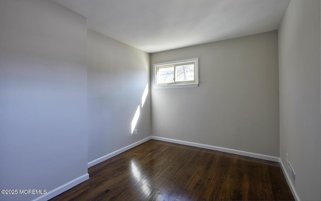 spare room featuring visible vents, baseboards, and dark wood-style flooring