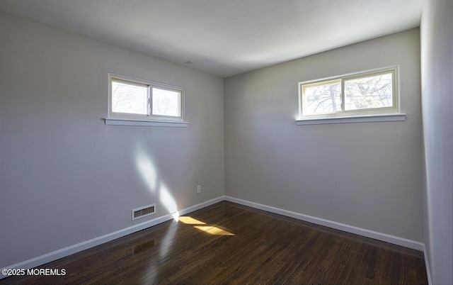 spare room featuring baseboards, plenty of natural light, visible vents, and dark wood-type flooring