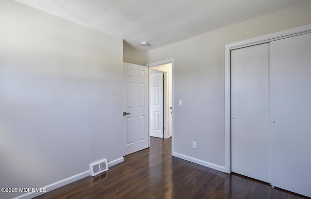 unfurnished bedroom featuring a closet, visible vents, baseboards, and wood finished floors