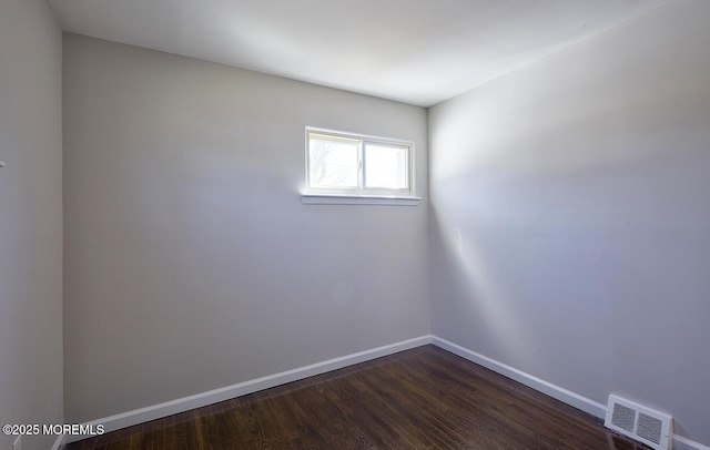 empty room featuring dark wood-style floors, visible vents, and baseboards