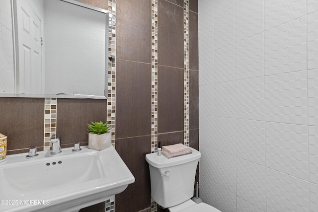 bathroom featuring a sink, toilet, and tile walls