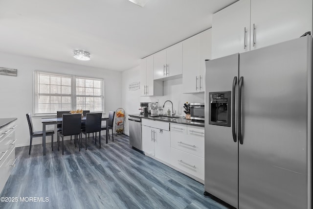 kitchen with dark wood finished floors, stainless steel appliances, dark countertops, white cabinetry, and a sink