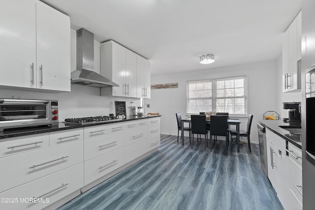 kitchen with a toaster, stainless steel appliances, dark countertops, dark wood-type flooring, and wall chimney exhaust hood